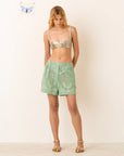 Woman wearing a silver sequin top and green shorts on a white background