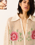 Woman wearing a beige knitted cardigan with floral patterns on a plain background