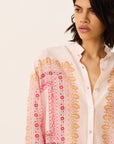 Woman wearing a white blouse with intricate pink and orange embroidery on a plain background
