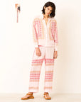 Woman wearing a light pink and white outfit with a patterned top and pants on a white background