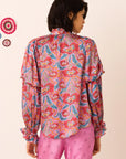 Person wearing a colorful patterned shirt and pink pants on a beige background