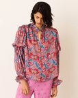 Woman wearing a colorful patterned blouse and pink pants on a white background