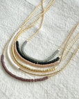 Set of layered necklaces with beaded and gold chains on a textured white surface