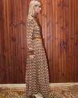 Alemais Sustainable Stefanie Knit Shirt Dress. Model is in a long, patterned dress standing against a wooden paneled wall.