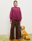 Person wearing a purple sweater with white polka dots and brown pants, standing next to a dog on a light-colored floor. Elia Mulberry Balloon Sweater