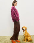 Woman in a pink sweater and brown pants standing next to a dog on a beige carpet. Elia Mulberry Balloon Sweater by Alemais