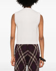 Person wearing a forte_forte cashmere wool English ribbed vest. It is white sleeveless top and patterned pants on a white background