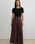 Woman wearing a black top and brown wide-leg pants against a plain background