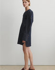 Woman wearing a dark denim dress standing against a plain white background