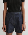 Person wearing dark denim shorts and a black top on a plain background