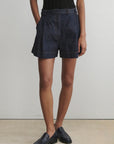 Person wearing dark denim shorts and black shoes on a plain background