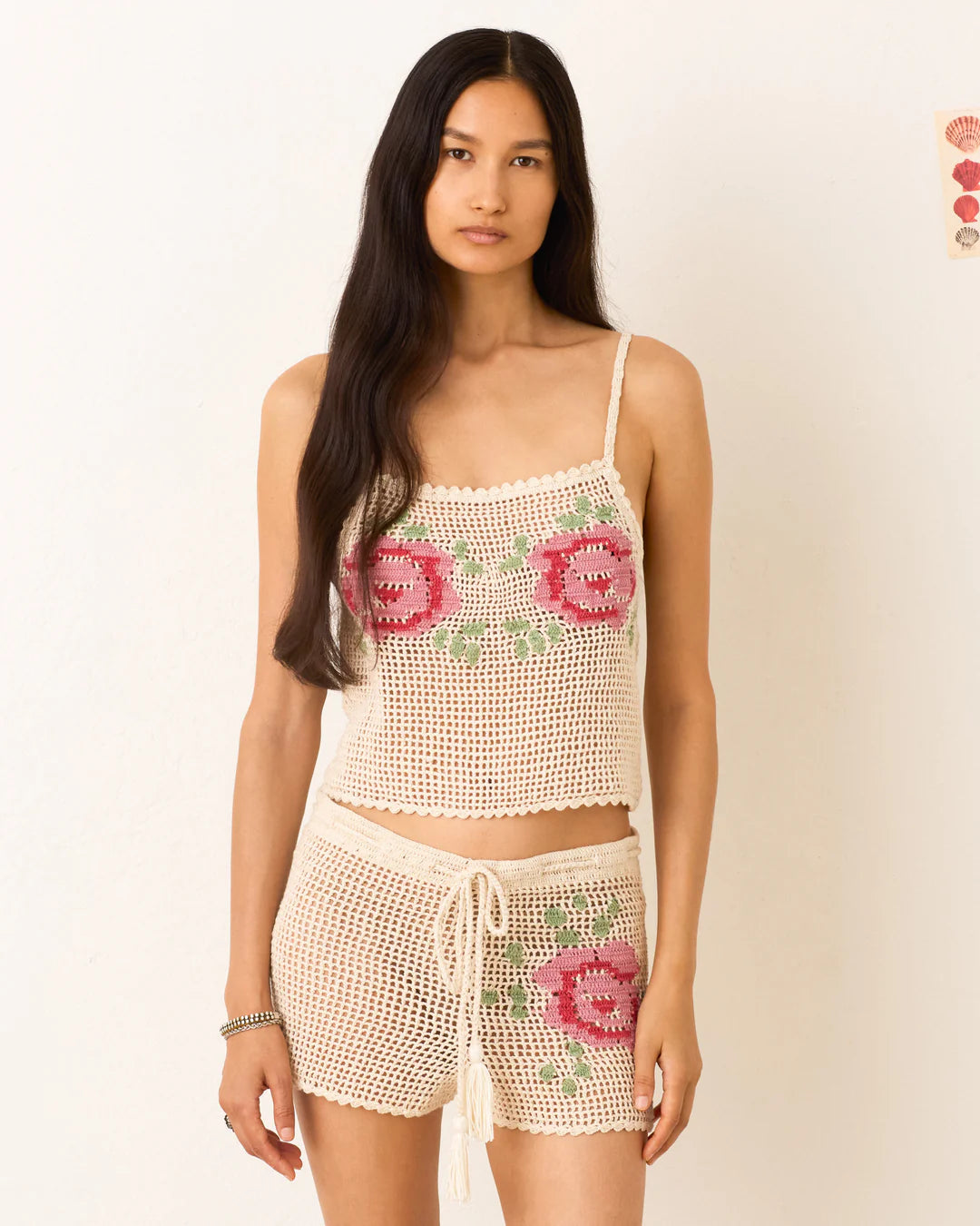 Woman wearing a crochet top and shorts set with floral patterns on a plain background