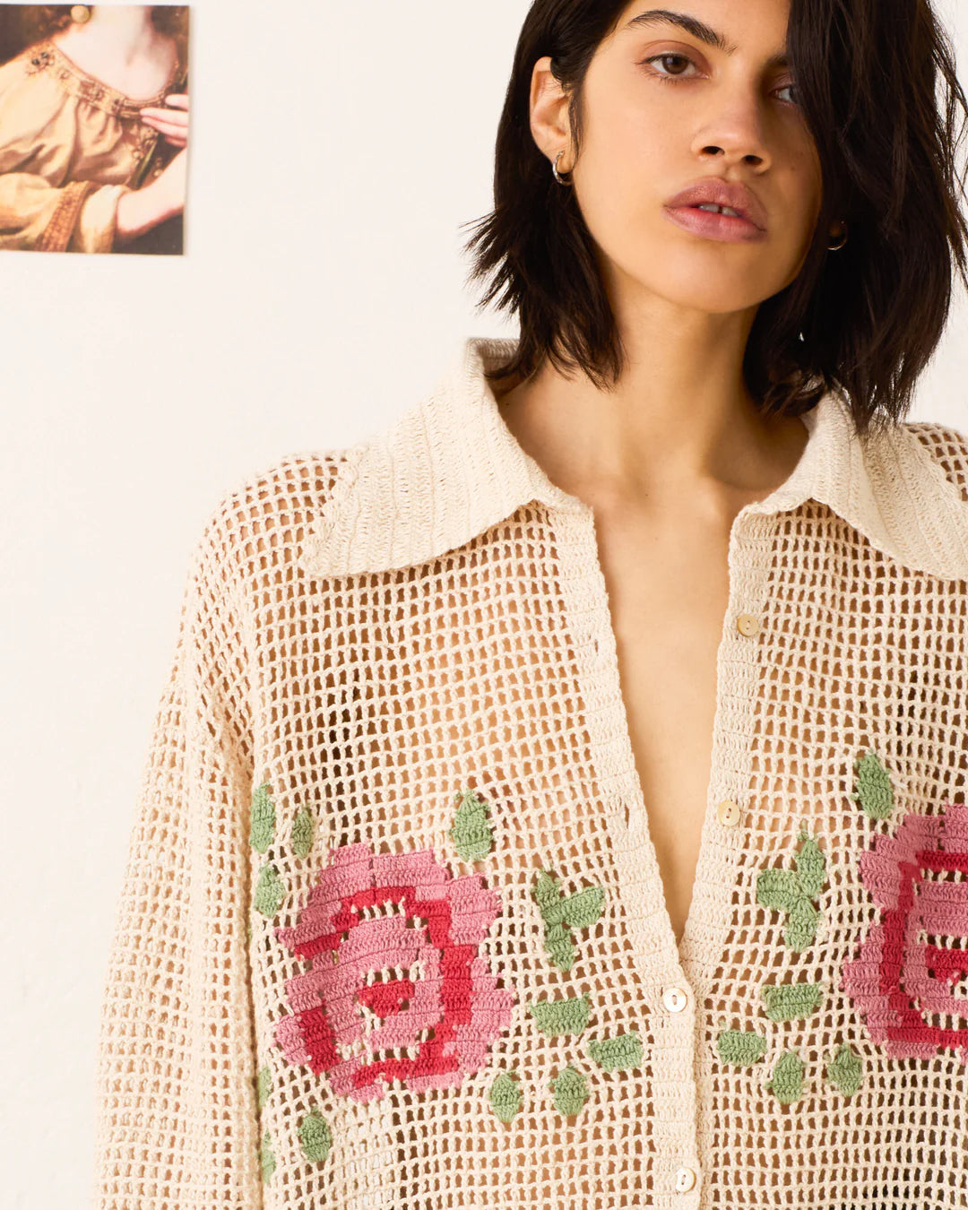 Woman wearing a beige knitted cardigan with floral patterns on a plain background