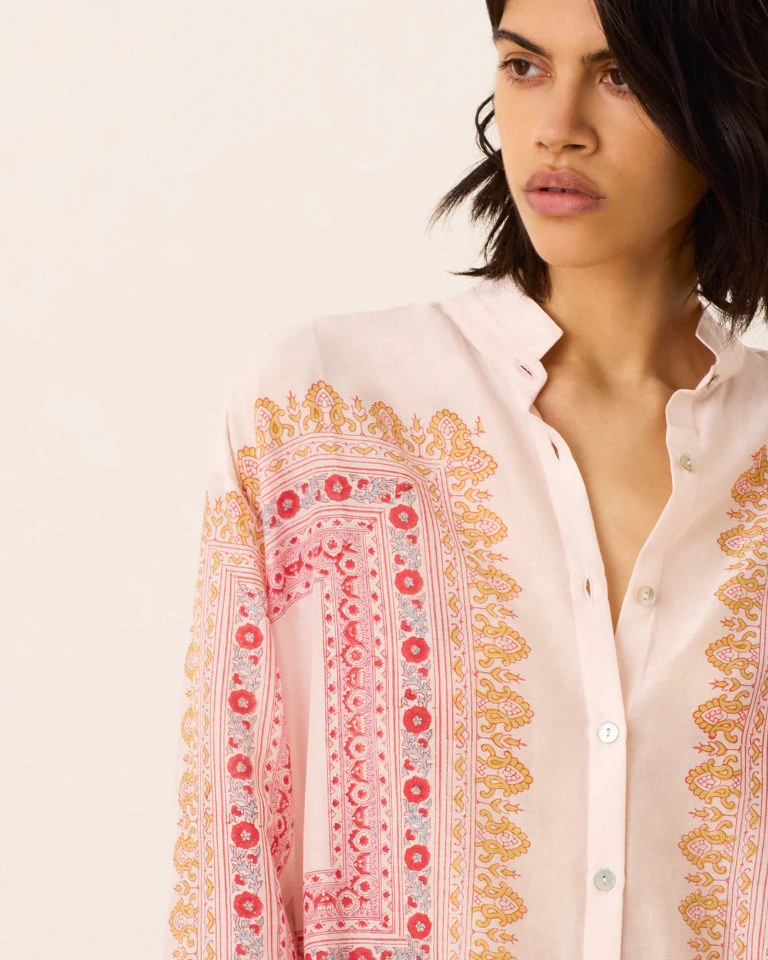 Woman wearing a white blouse with intricate pink and orange embroidery on a plain background