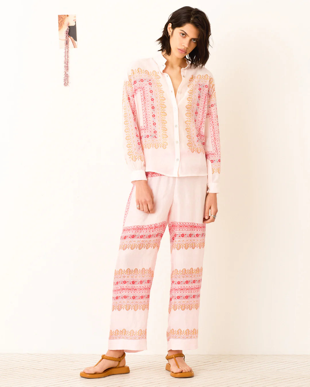 Woman wearing a light pink and white outfit with a patterned top and pants on a white background