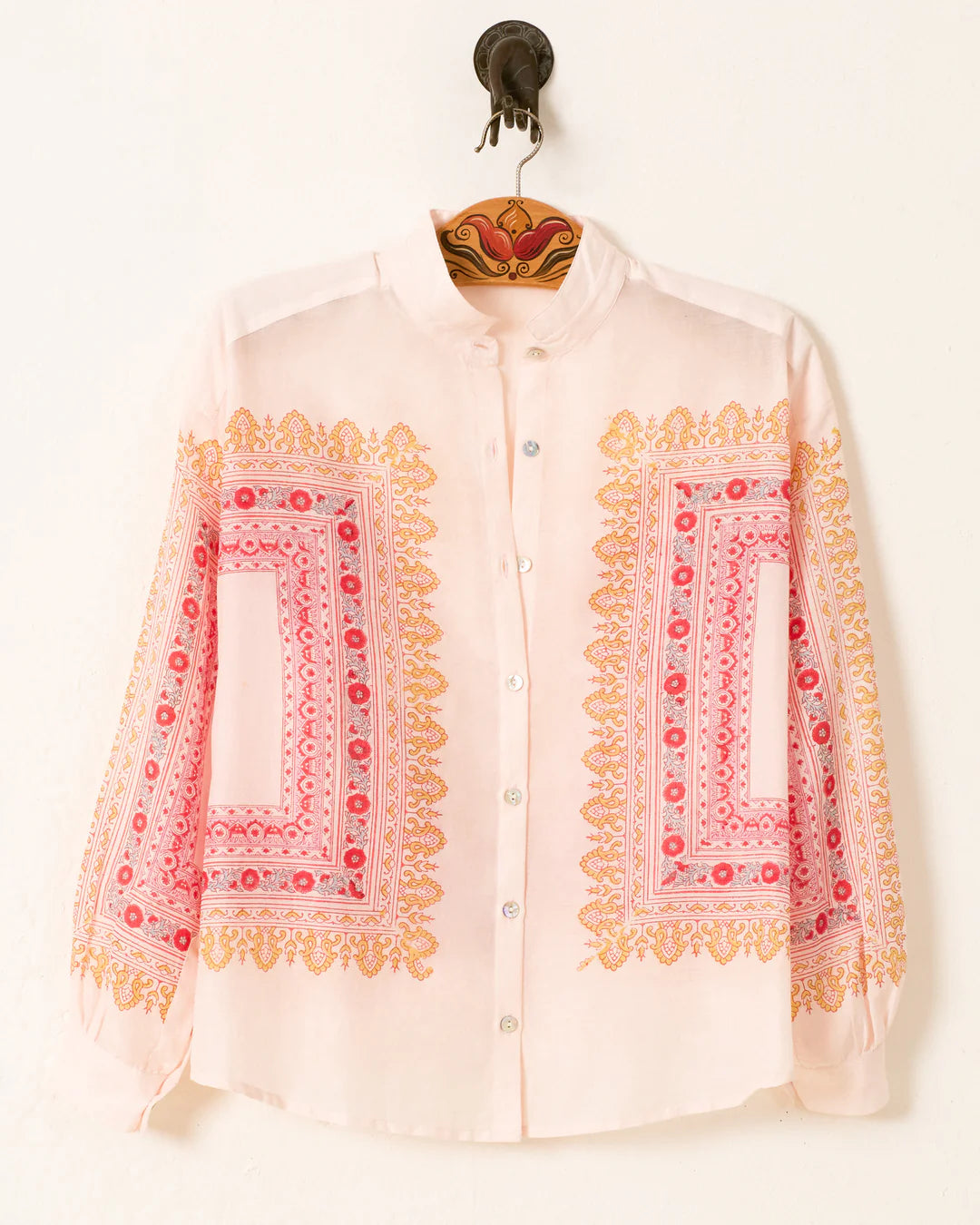 White shirt with pink and yellow embroidery on a hanger against a white background