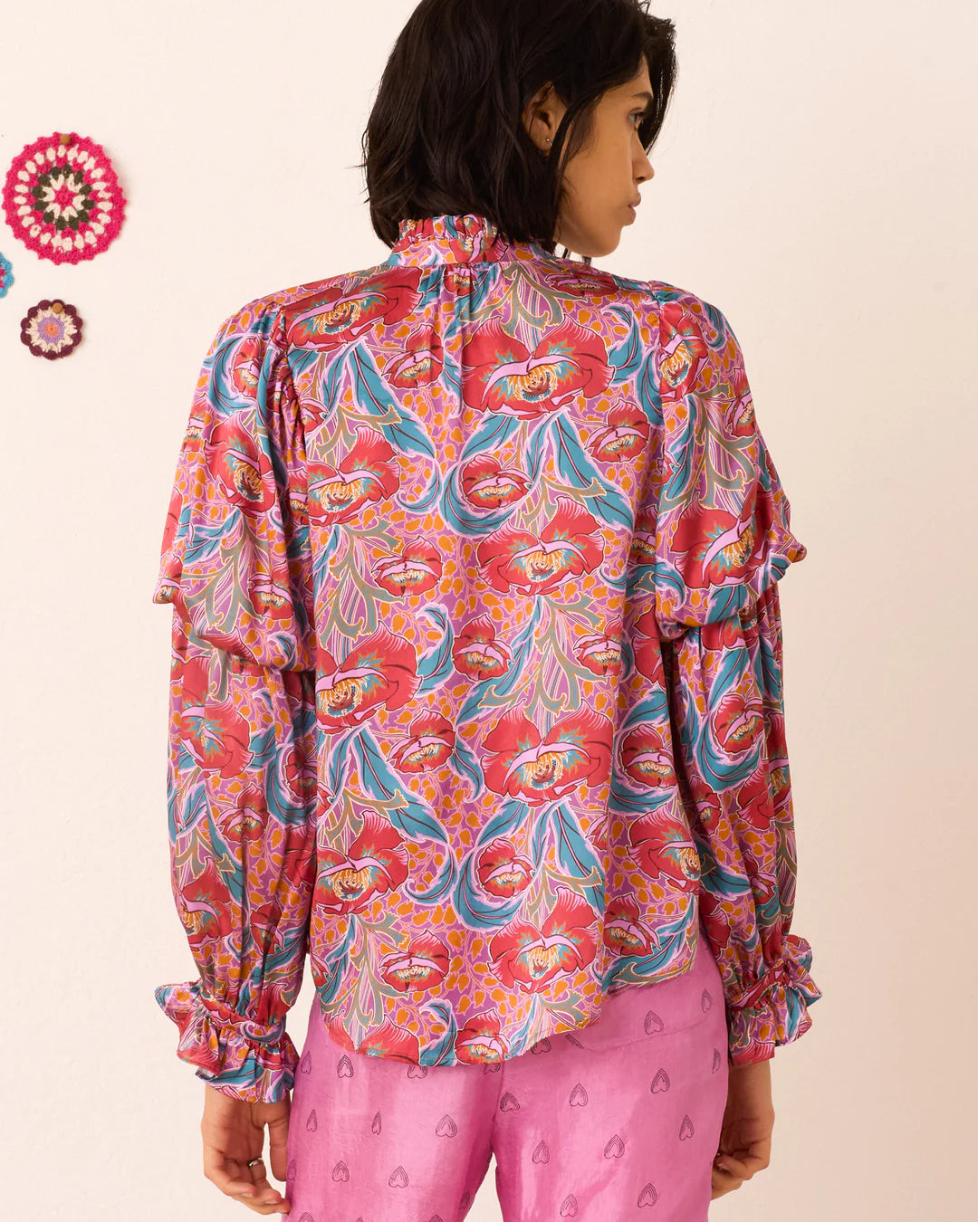 Person wearing a colorful patterned shirt and pink pants on a beige background