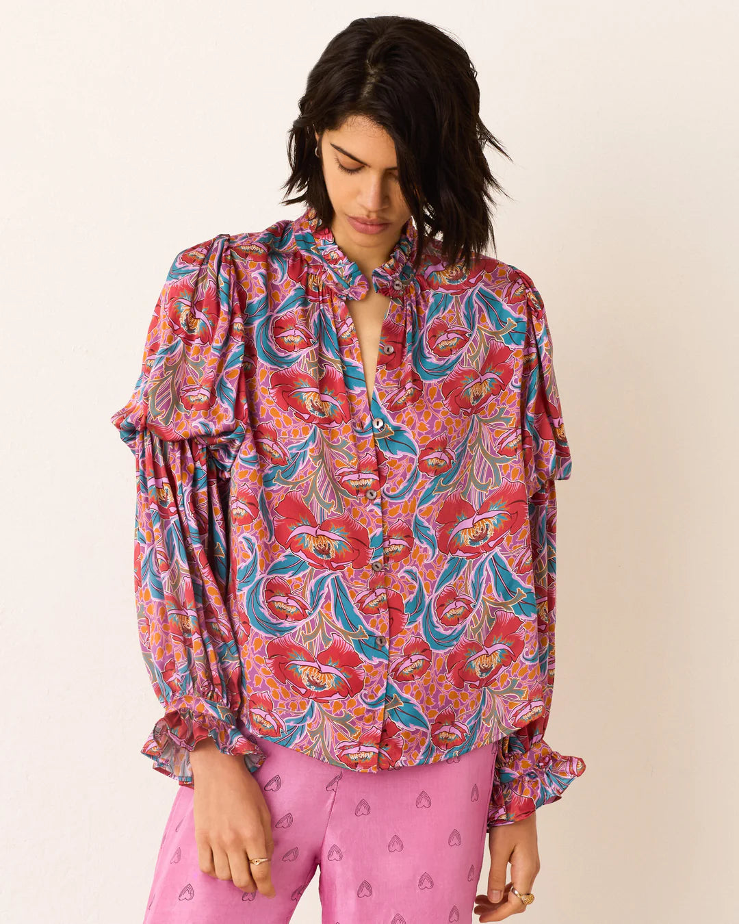 Woman wearing a colorful patterned blouse and pink pants on a white background