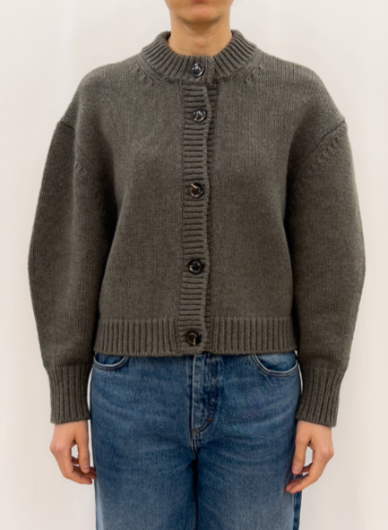 Person wearing a gray knitted cardigan and blue jeans on a white background