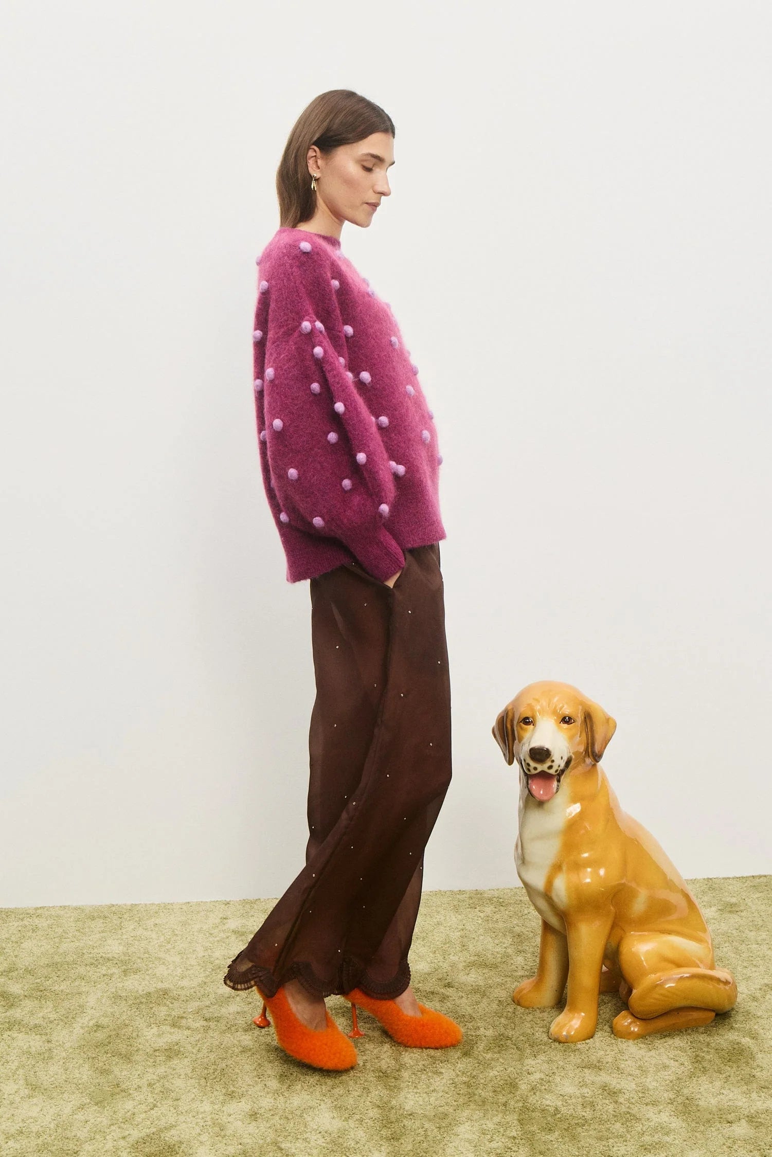 Woman in a pink sweater and brown pants standing next to a dog on a beige carpet.  Elia Mulberry Balloon Sweater by Alemais