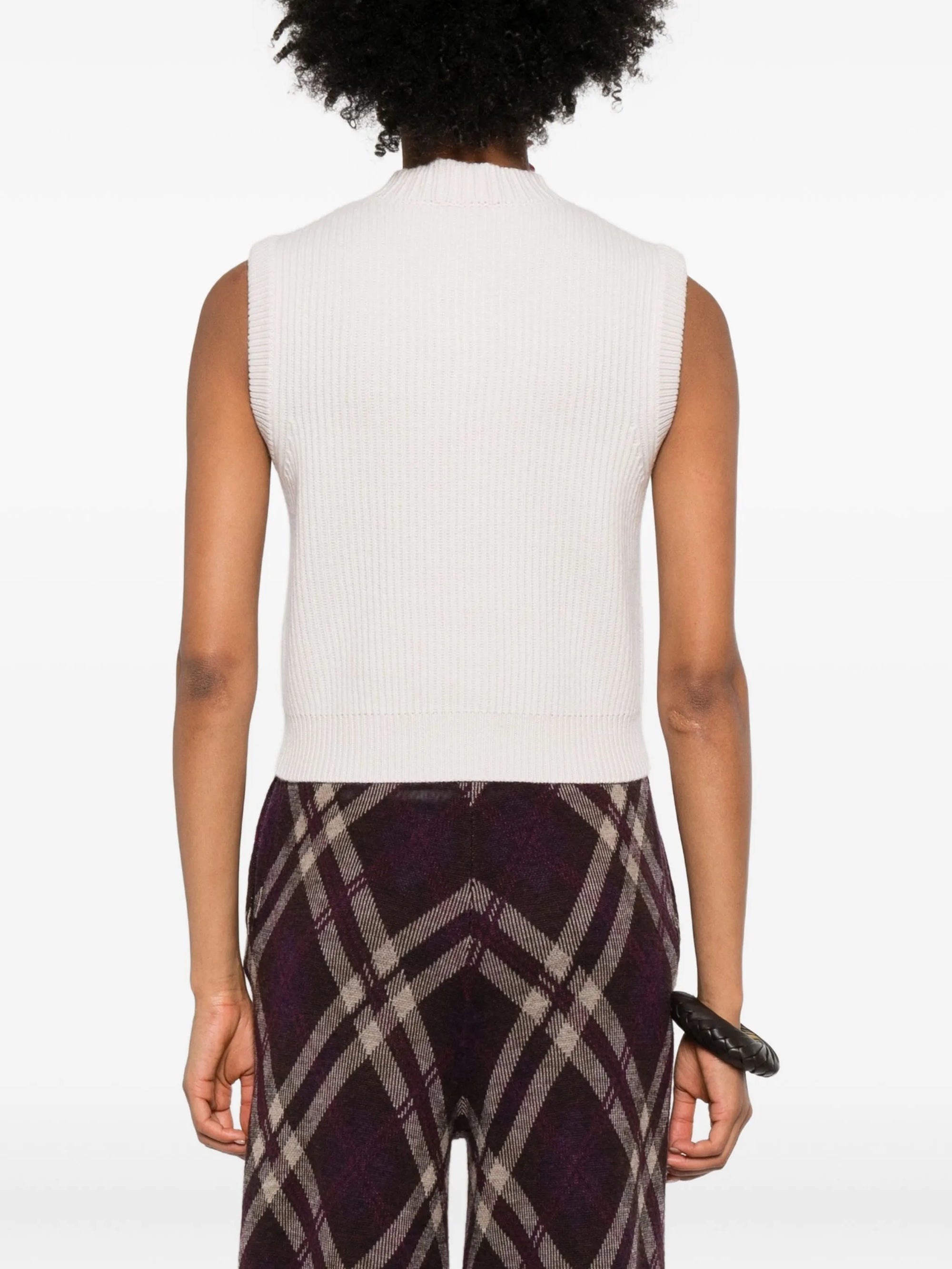 Person wearing a forte_forte cashmere wool English ribbed vest. It is white sleeveless top and patterned pants on a white background