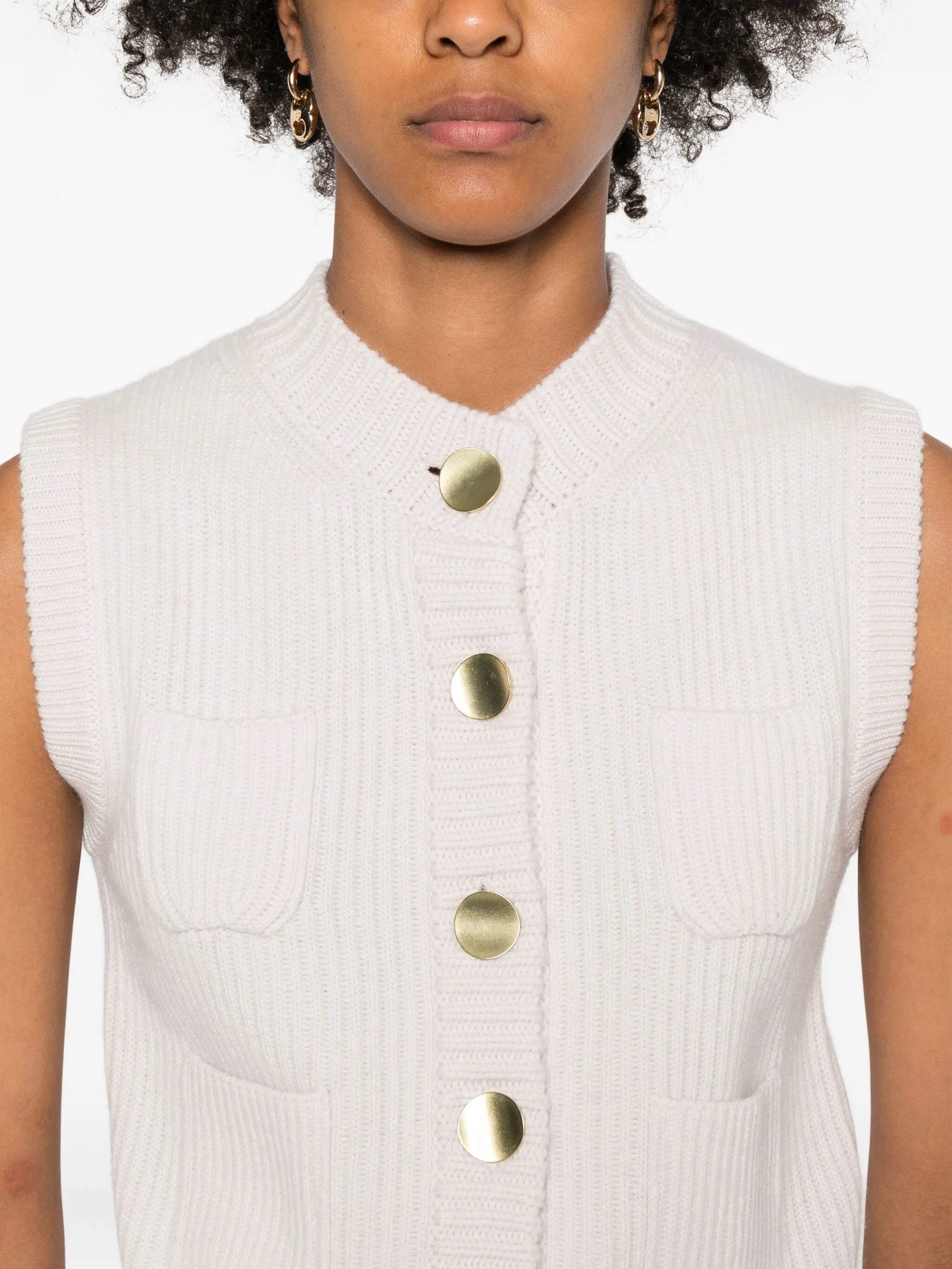 White sleeveless top with gold buttons worn by a person on a white background