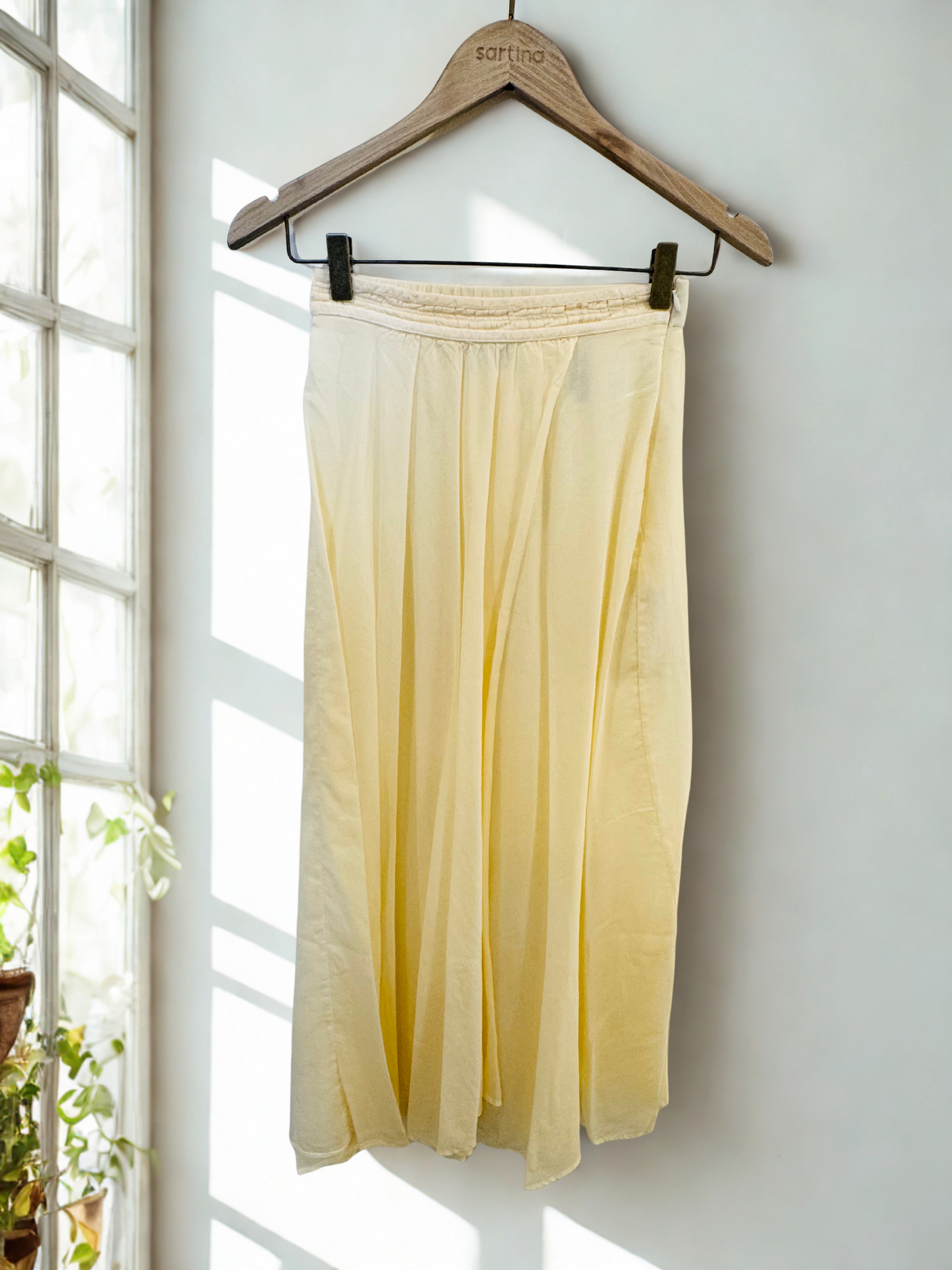 Yellow skirt hanging on a wooden hanger against a white wall with natural light by forte_forte