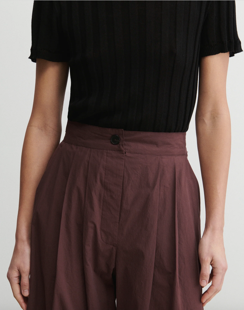 Person wearing a black top and brown pants on a plain background