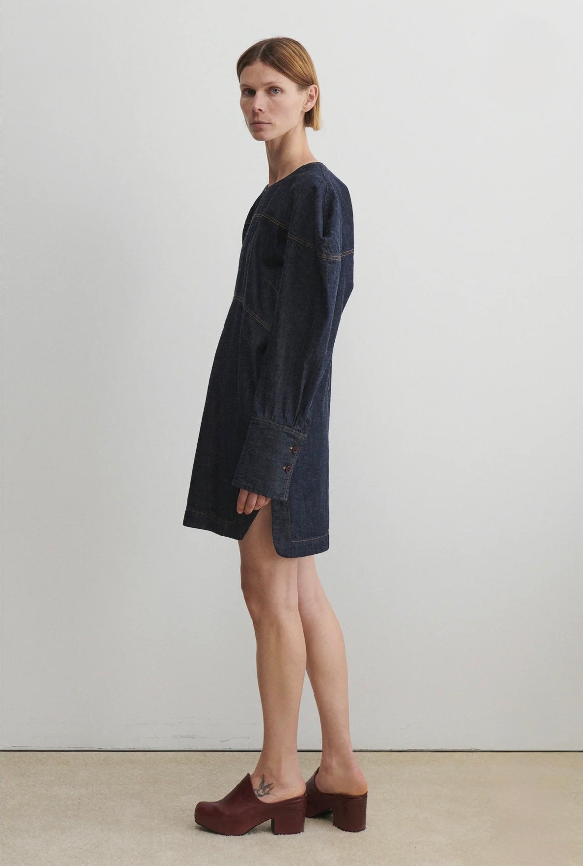 Woman wearing a dark denim dress standing against a plain white background