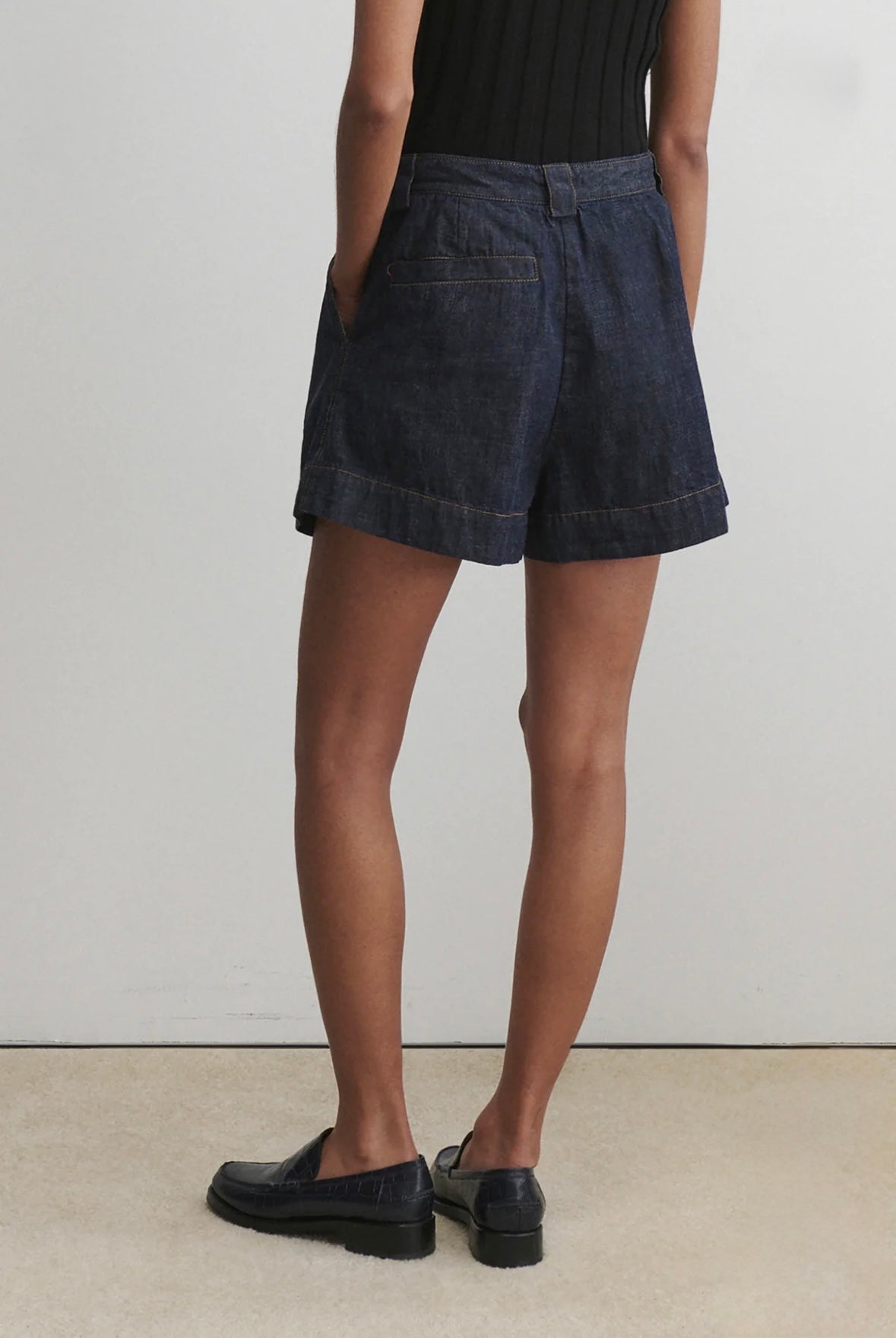 Person wearing dark denim shorts on a plain background