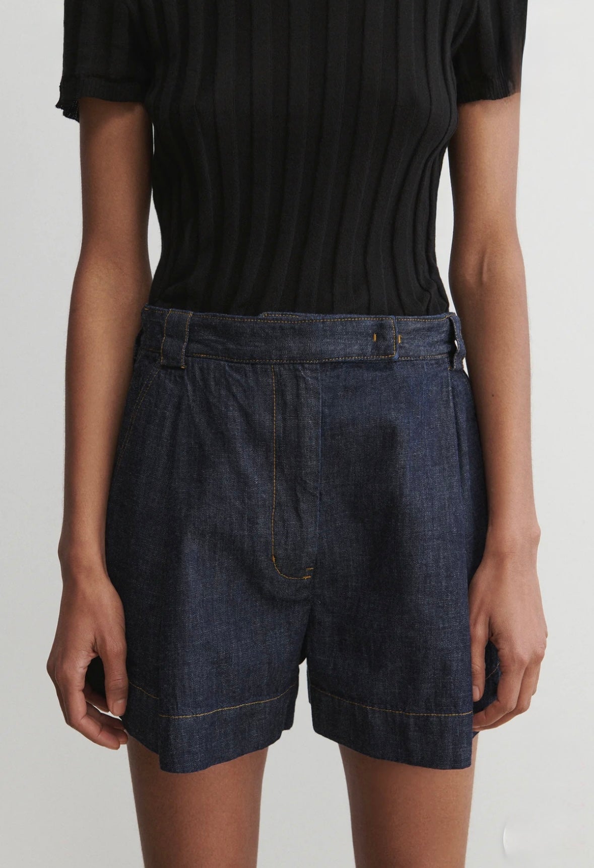 Person wearing dark denim shorts and a black top on a plain background