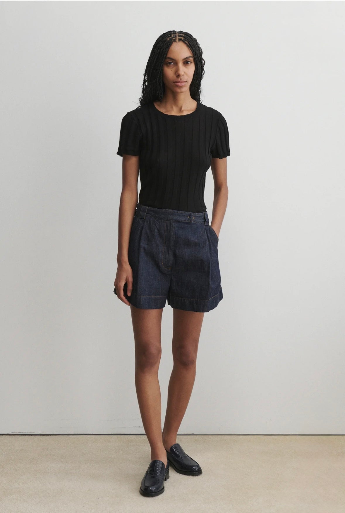 Person wearing a black t-shirt and dark shorts against a plain background
